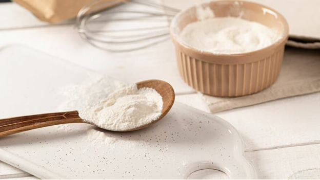 A wooden spoon and bowl of flour on the table.